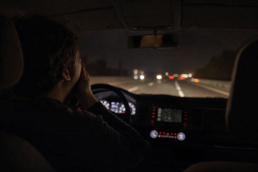 Vermoeide bestuurder aan het stuur, naast een beschadigde auto