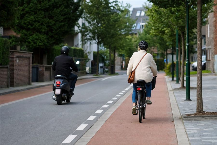 Een bromfiets en een fietser die samen op de rijbaan rijden