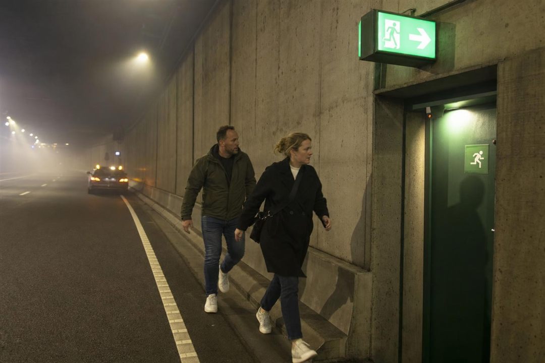 Twee inzittenden lopen in een tunnel naar de nooduitgang, aangeduid met een groen bord