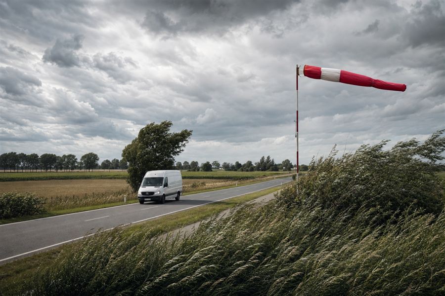 Bestelwagen in harde wind, met een strakke windzak en gebogen bomen