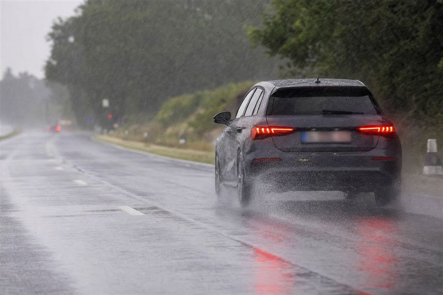 Auto in een zware regenbui, met water dat onder de banden wegspuit