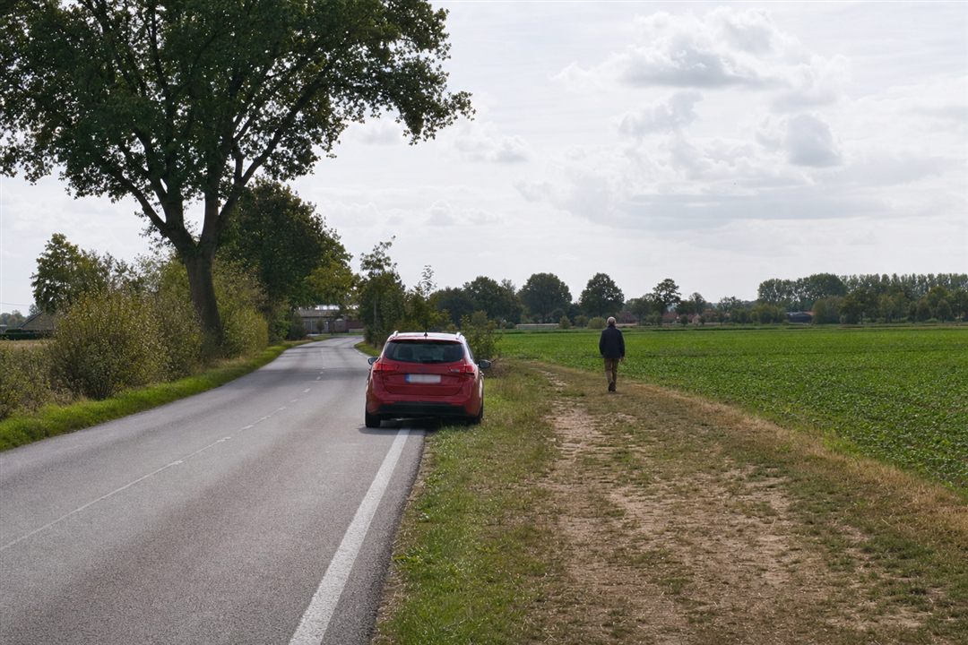 Een voetganger passeert langs de buitenkant van een auto op de berm