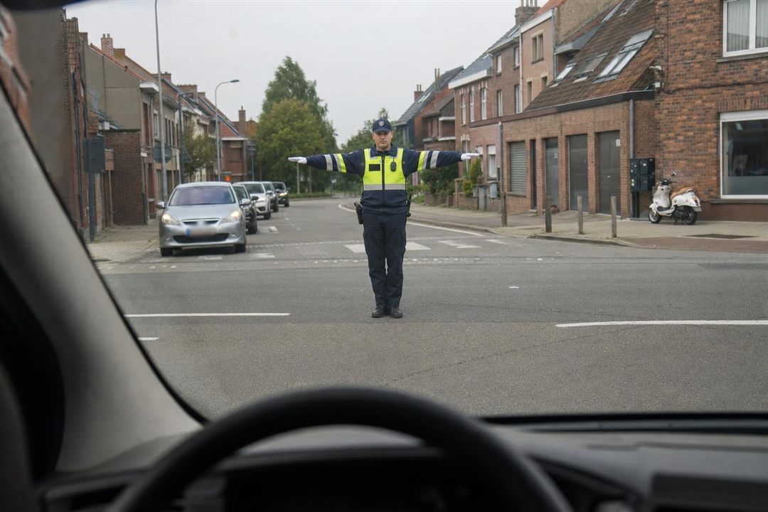 Bevoegd persoon op een kruispunt met de armen horizontaal uitgestrekt, gezien door de voorruit