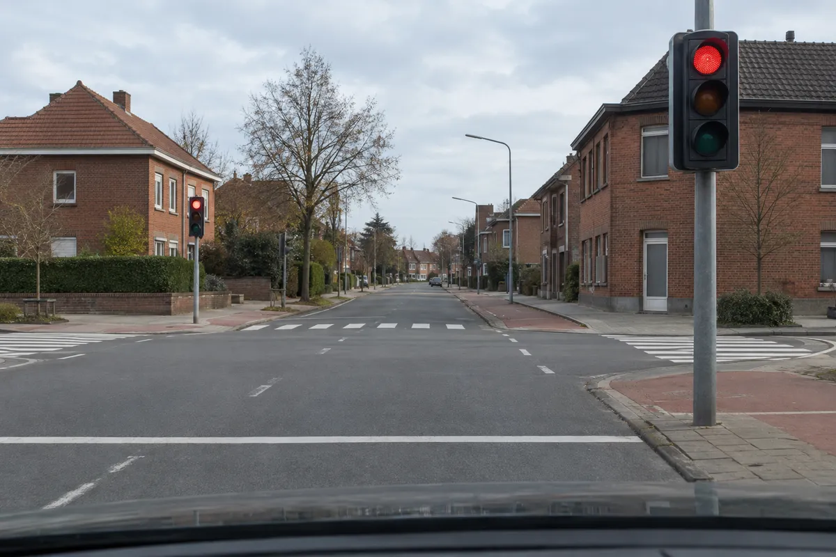 Een driekleurig verkeerslicht met rood boven, oranjegeel in het midden en groen onder, en de stopstreep op het wegdek.