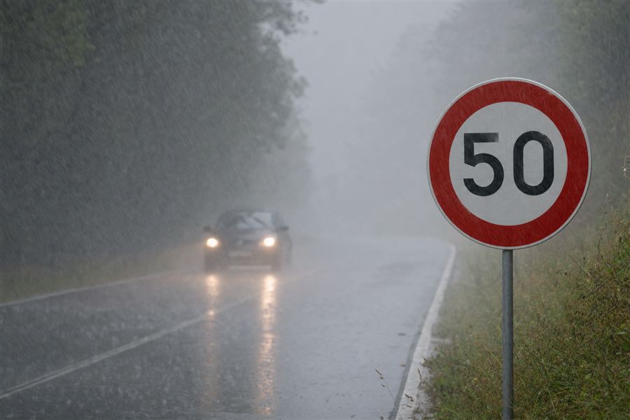 Twee auto's in felle regen, bij een bord dat de snelheid beperkt