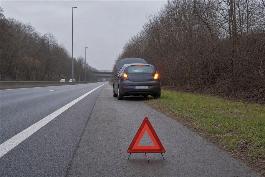 Auto met pech en open motorkap, aangeduid met een gevaarsdriehoek, terwijl een andere auto voorbijrijdt
