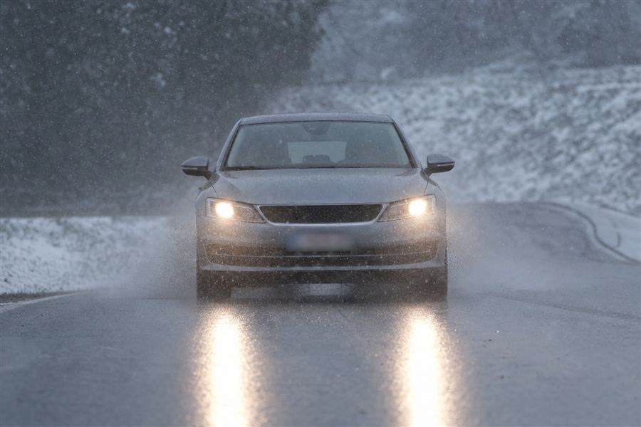 Auto met lichten aan bij gemengde sneeuw en regen